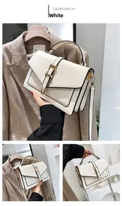 Detail of white structured crossbody bag featuring black edges and gold buckle closure