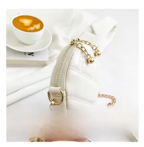 Détail de la fermeture éclair dorée et du motif matelassé sur un petit sac crème