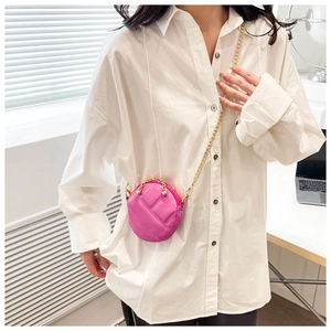 Détail d'un mini sac rond matelassé rose avec une bandoulière en chaîne dorée sur bureau