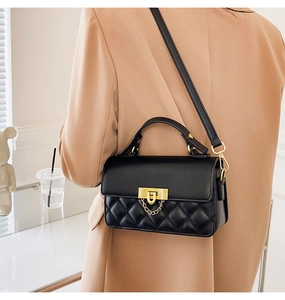 Detail einer schwarzen Stepptasche mit goldenem Schloss auf einem beigen Blazer