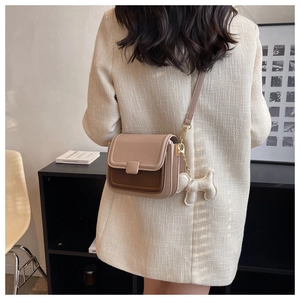 Detail of a beige and brown crossbody bag with a plush dog charm and slim shoulder strap