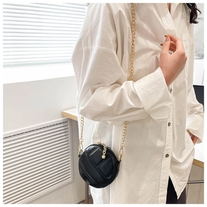 Gros plan du mini sac rond noir matelassé avec bandoulière chaîne dorée sur chemise blanche