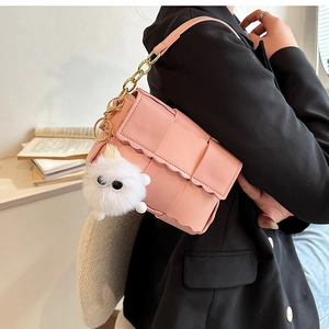 Detail of pink woven crossbody bag with wavy flap edge and cute plush monster charm