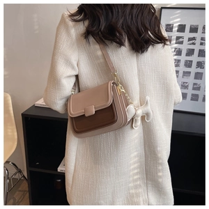 Detail of color-block crossbody bag with puppy charm worn over a white tweed jacket