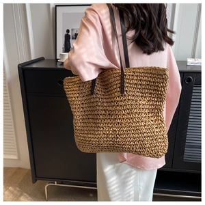 Large woven straw tote bag with brown straps shown on a model in a modern home interior