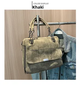 Detail of khaki tote bag with quilted stitching and metal chain handles on wooden backdrop