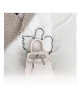 Detail of cream mini handbag featuring a sparkling rhinestone bow and silver chain strap