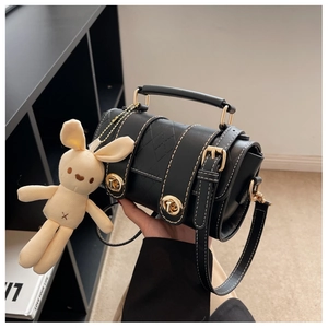 Close-up of black quilted leather crossbody bag with gold buckle and cute rabbit pendant