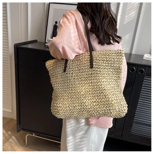 Detail of hand-woven straw tote bag featuring brown leather straps on a pink shirt model