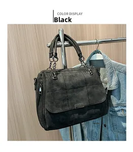Detail of black suede tote bag with cross stitching, metal buckle, and chain strap handle