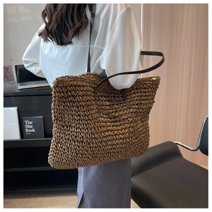 Detail of a large dark brown woven straw tote bag worn over the shoulder by a model