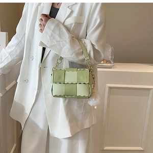 Detail of light green woven crossbody bag with gold chain strap and plush ball charm