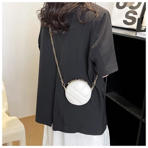 Détail d'un mini sac rond blanc matelassé avec bandoulière chaîne dorée sur un mannequin