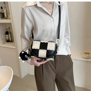 Close-up of a black and white checkerboard crossbody bag with wavy edge and plush charm