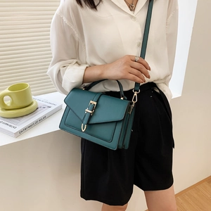 Deep green rectangular handbag with gold buckle and adjustable strap in a minimalist setting
