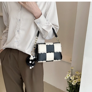Detail of checkered crossbody bag with wavy edges, chain strap and a cute doll charm