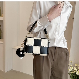 Detail of checkered shoulder bag featuring wavy edges, gold chains and a fur pompom charm