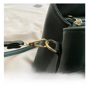 Close-up of golden hardware hooks and zippers on dark green litchi grain leather handbag