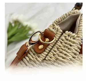 Detail of gold metal hook and brown leather strap on a beige woven straw bag