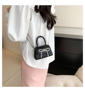 Detail of black crossbody bag with silver rhinestone bow and metal chain strap