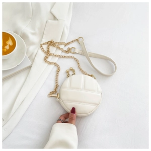 Vue détaillée de dessus d'un sac rond matelassé blanc avec chaîne dorée et accessoires