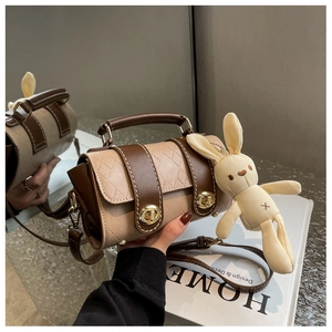 Detail of quilted beige cylinder bag featuring coffee trim and a cute rabbit charm