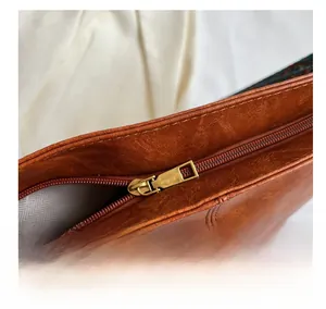 Detailed close-up of the smooth metal zipper and premium brown leather texture on handbag