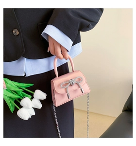 Mini light pink crossbody bag with rhinestone bow and silver chain held by a model