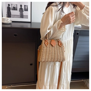 Detail of woven straw handbag with brown leather trim and bamboo-style top handle