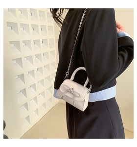 Detail of cream mini crossbody bag with a sparkling rhinestone bow and silver chain strap