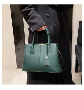 Detail of dark green matte leather tote bag with vertical stitching and gold hardware accents