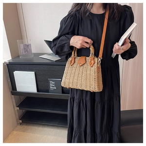 Detail of hand-woven straw bag featuring a bamboo top handle and brown leather flap cover