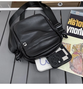Detail of black faux leather crossbody bag with adjustable strap and metal hardware