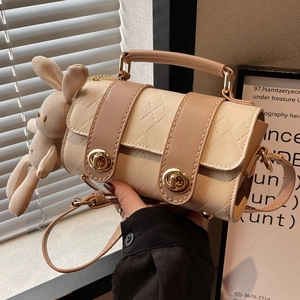 Off-white cylindrical crossbody bag with diamond quilting and a plush rabbit charm