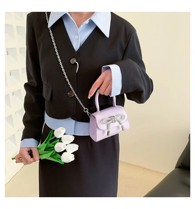 Lavender mini crossbody bag with rhinestone bow detail shown on shoulder with suit
