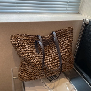 Minimalist straw woven tote bag with brown leather straps in a soft sunlit indoor setting