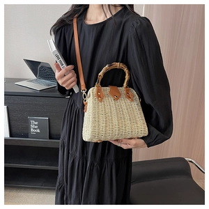 Detail of straw tote bag featuring bamboo handle and adjustable brown leather strap