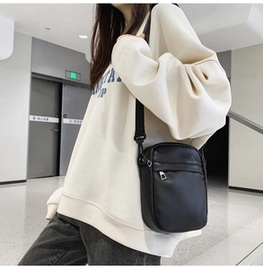 Model wearing a black PU leather crossbody phone bag with wide adjustable shoulder strap