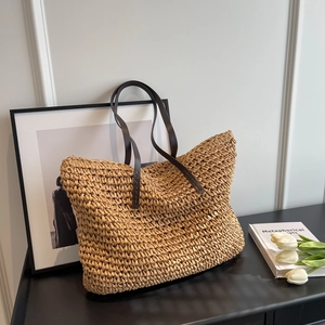Handcrafted straw tote bag with brown leather handles in a rustic minimalist interior