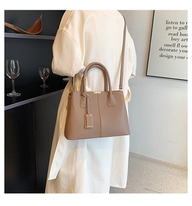 Taupe leather tote bag with top handles and adjustable strap shown on shoulder