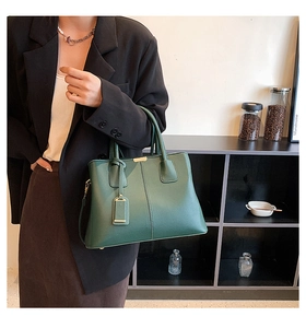 Close-up of a dark green lychee grain leather handbag with minimalist metal bar detail