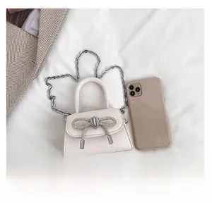 Mini off-white crossbody bag with rhinestone bow and chain strap next to a smartphone