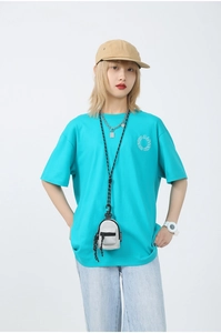 Gros plan d'un t-shirt bleu ciel avec mini sacoche grise et logo blanc sur fond neutre