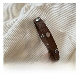 Detail view of a brown pebbled leather strap with silver metallic round studs and texture