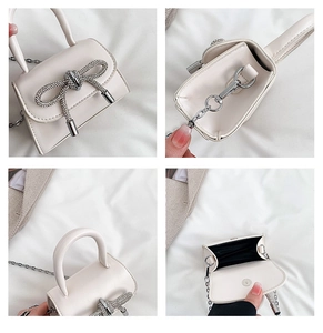 Detail view of mini cream handbag showing rhinestone bow, silver chain, and inner compartment