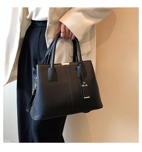 Close-up of black lychee grain tote bag with gold hardware held by a model in a white suit