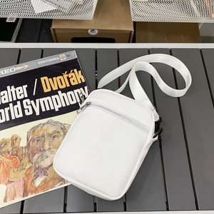 Minimalist white small crossbody bag with adjustable strap on a textured outdoor table