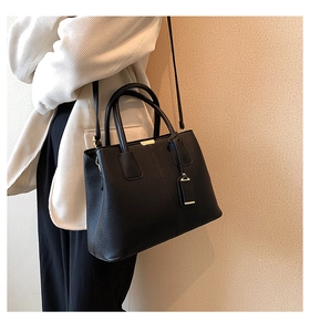 Chic black litchi texture handbag with gold metal zipper shown on shoulder of a model