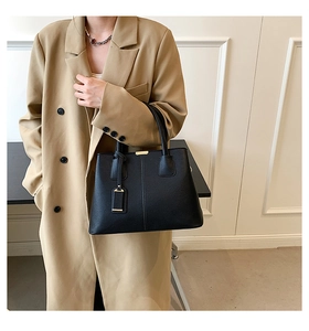 Close-up of black lychee grain handbag with gold hardware styled with a khaki coat