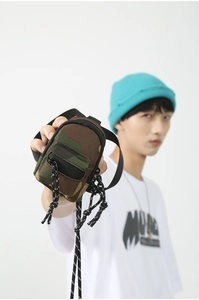 Détail d'une mini pochette camouflage avec fermeture éclair noire tenue par un mannequin